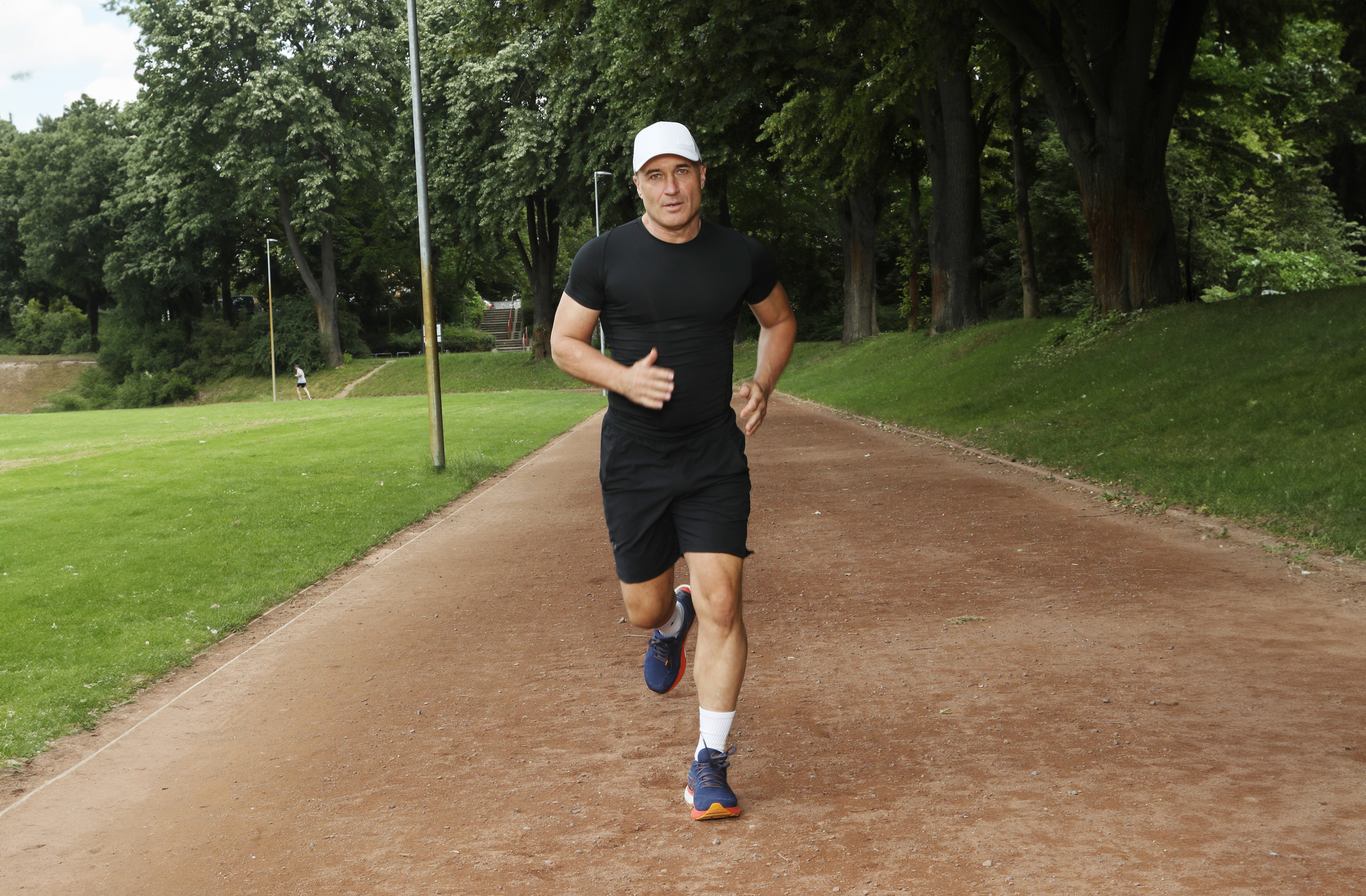 Scarpe da Corsa Uomini – Modelli Sportivi da 10 km Uomo che corre su un sentiero forestale, indossando abbigliamento sportivo nero e scarpe da corsa blu.