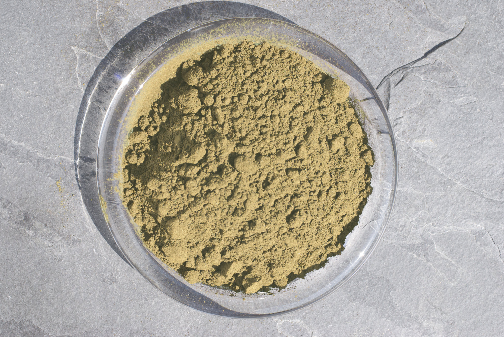 Polvere di erbe – 100 g Polvere di erbe fine in una ciotola trasparente, marrone-verde, vista dall'alto.
