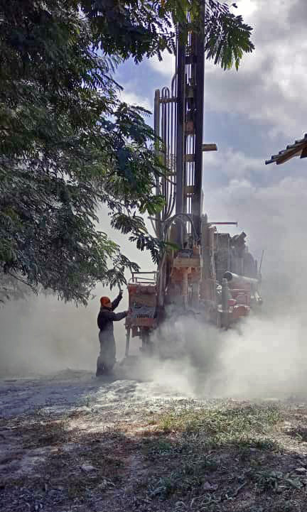 Trivellatrice – Perforazione acqua in loco Lavoratore manovra una trivellatrice in un ambiente polveroso, con alberi sullo sfondo.
